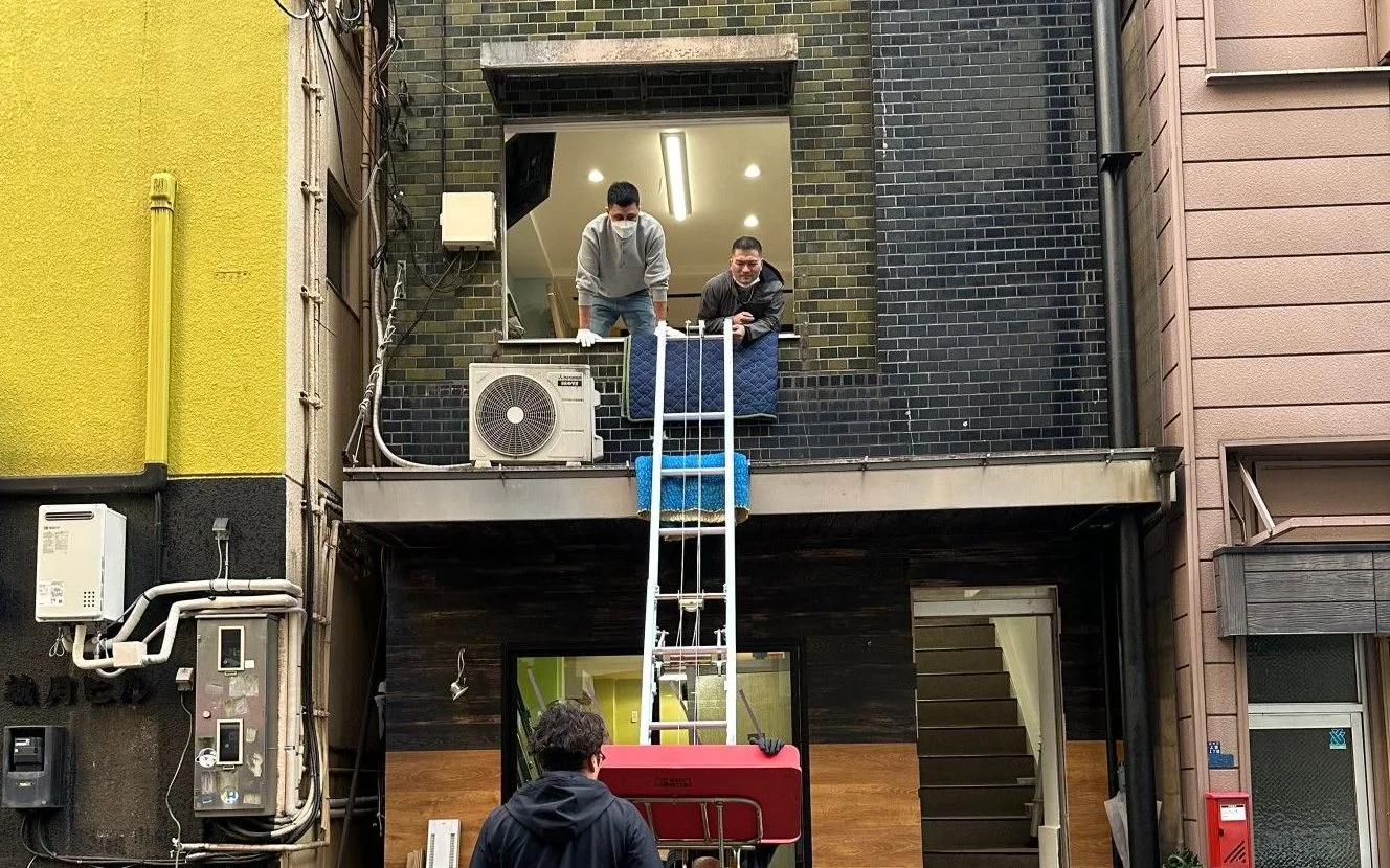 Staff installing a powered ladder along the exterior wall and bringing a large piece of furniture in through a second-floor window