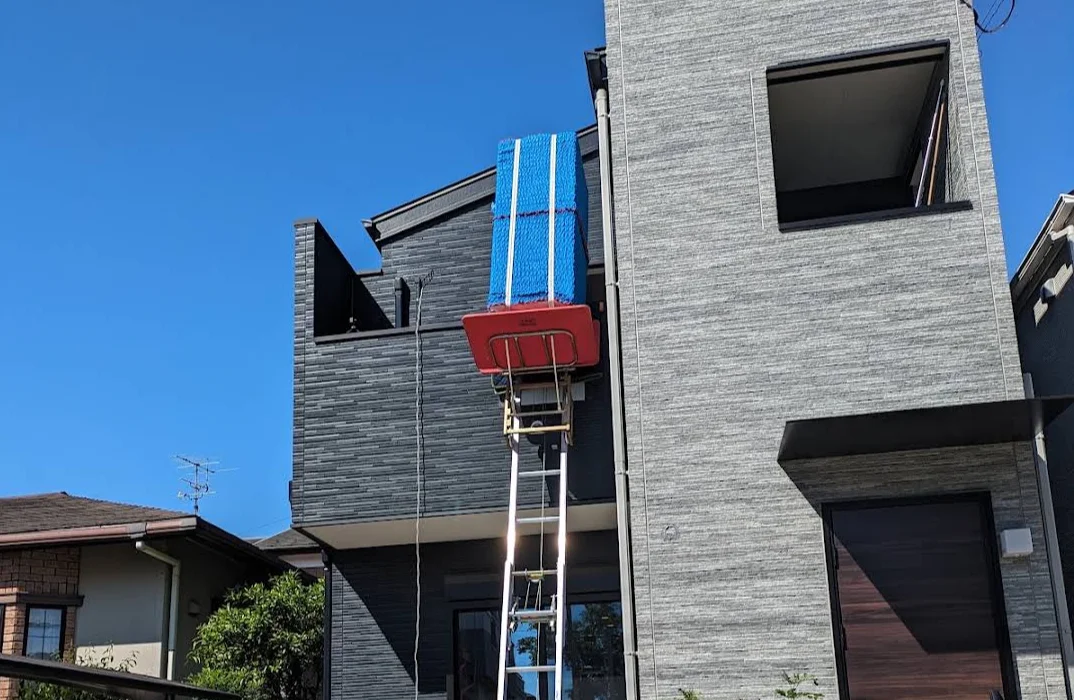 Workers hoisting a large bedding item with a powered ladder and bringing it in through a building window