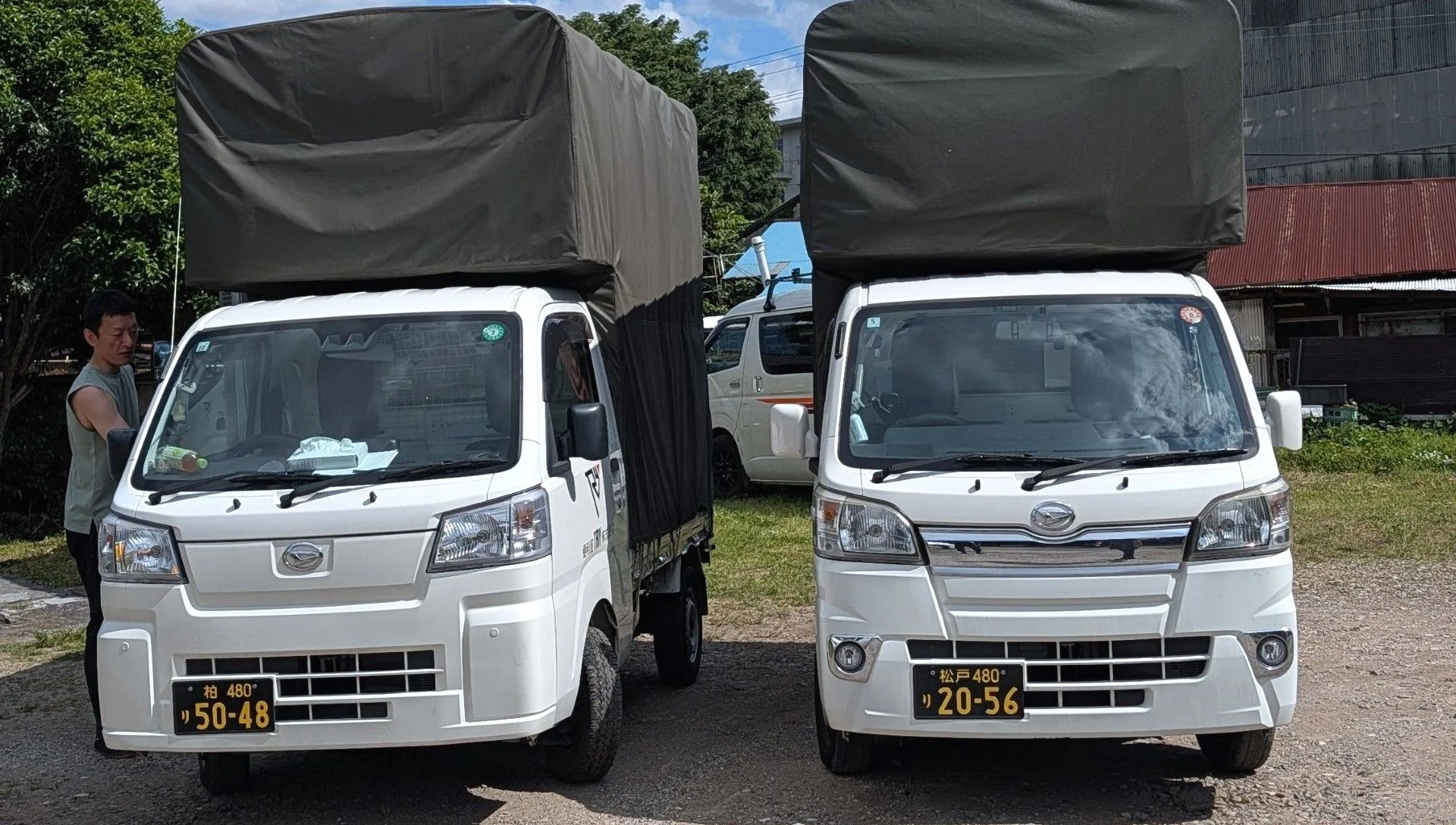 Two white kei trucks parked side by side, each with a green cover