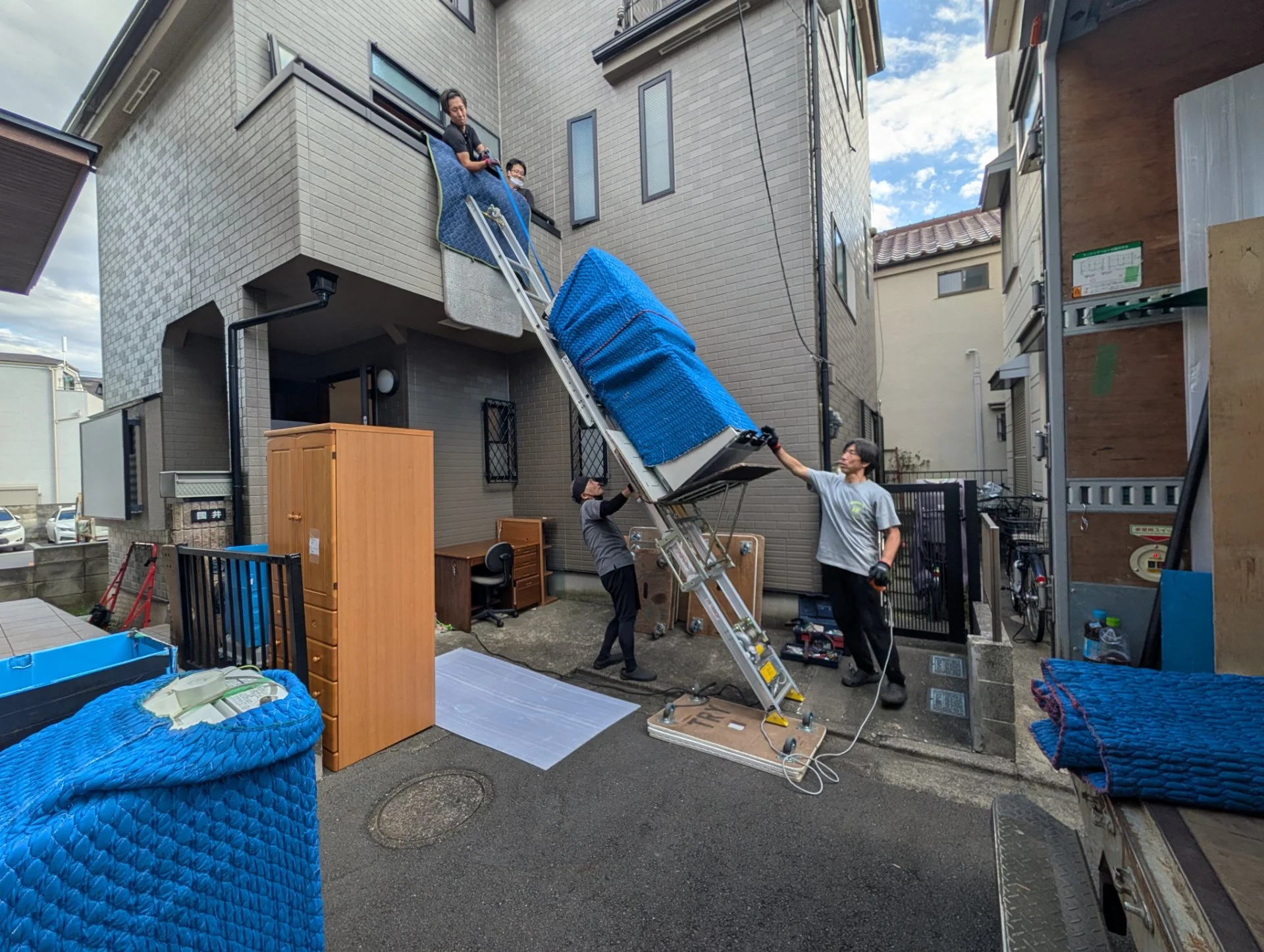 ラダーリフトを使い、養生した大型の荷物を2階バルコニーへ運び上げる作業員